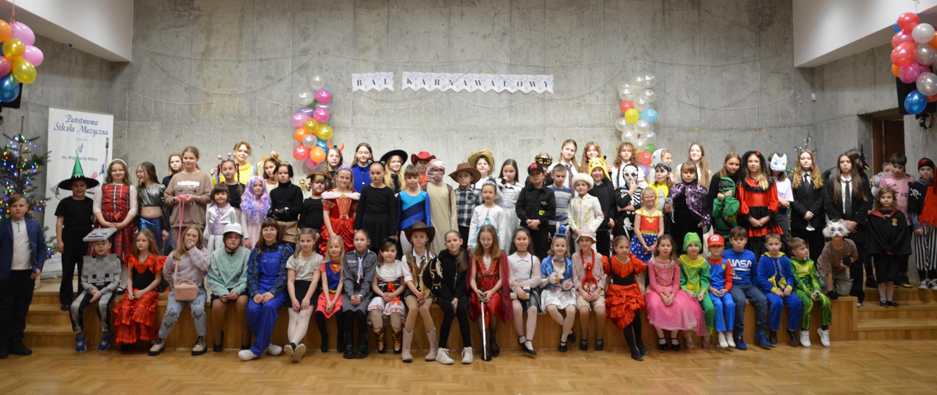 Grupa uczniów w strojach karnawałowych stoi na scenie sali koncertowej szkoły