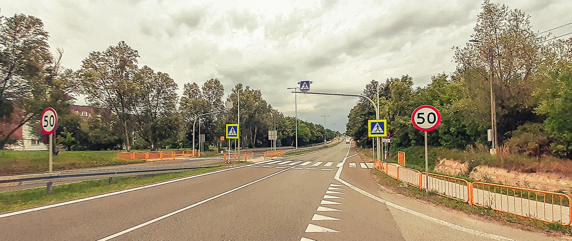 Fotografia przejścia dla pieszych na terenie woj. śląskiego wyposażonego w dedykowane oświetlenie drogowe, szczeblinowe bariery wygrodzeniowe oraz podświetlony i wyniesiony nad przejście dla pieszych znak D6 „przejście dla pieszych” z pulsującą sygnalizacją ostrzegawczą w kolorze żółtym. 