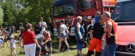 Na zdjęciu samochód ratowniczo-gaśniczy z JRG 2. Samochód czerwony, lampy niebieskie, ostrzegawcze. Wokół ludzie, którzy uczestniczą w Dniu Dziecka. Zdjęcie wykonane w ciągu dnia.