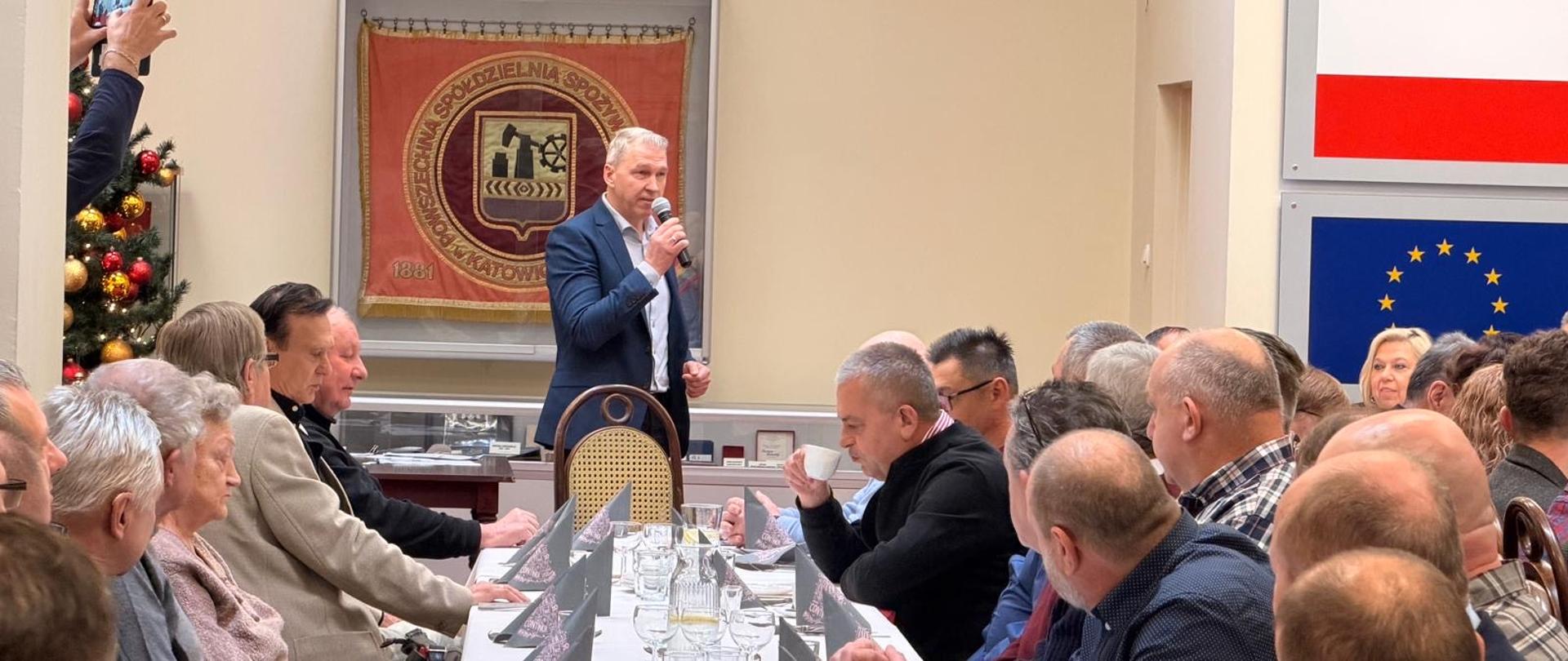Emeryci i renciści siedzący przy stołach w sali bankietowej Społem podczas przemówienia Komendanta Miejskiego PSP w Katowicach
