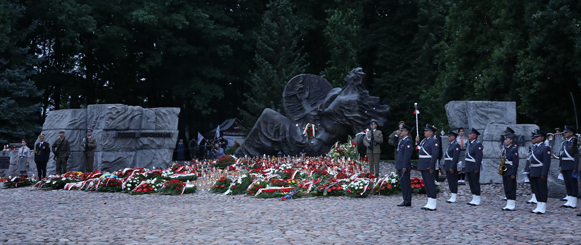 Widok na Pomnik "Polegli - Niepokonani" z zapalonymi zniczami i złożonymi kwiatami.