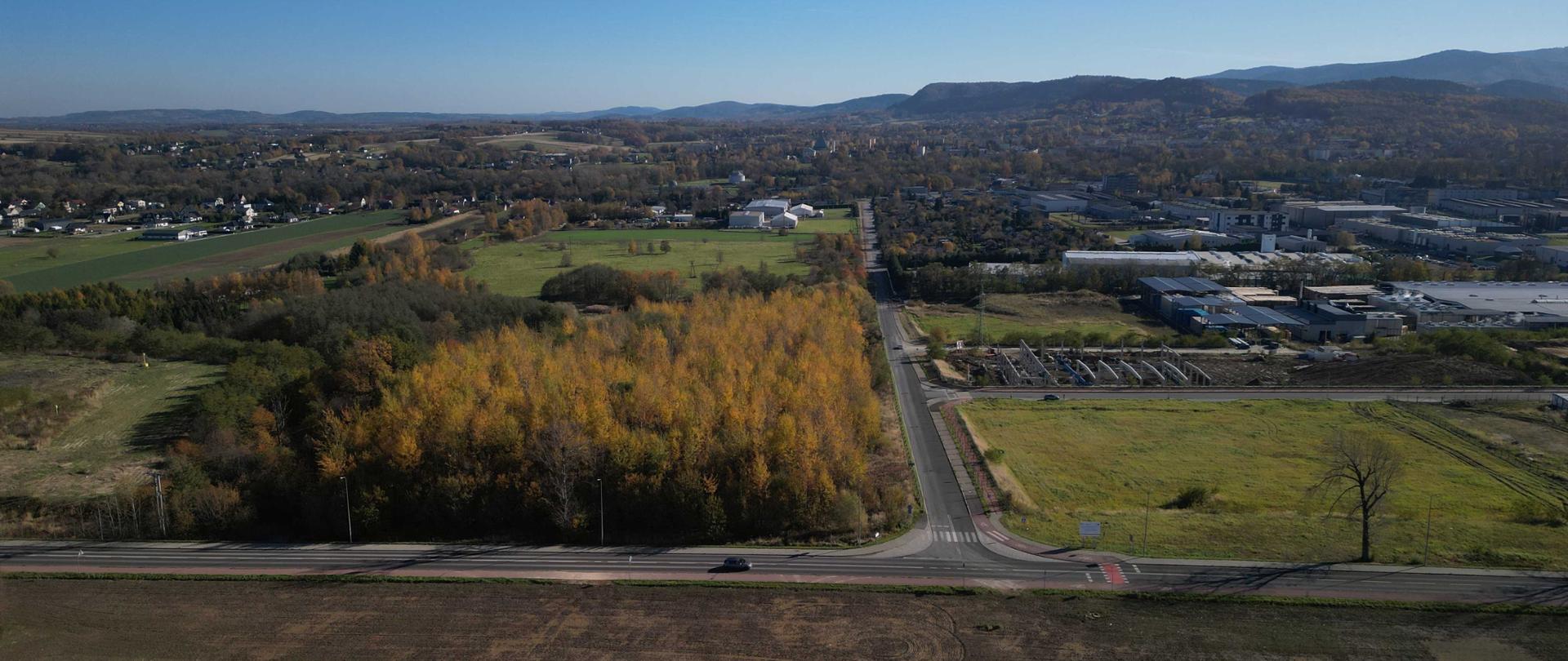 Teren BDI w Andrychowie, na pierwszym planie pole, dalej niewielki las i rozproszone zabudowania, w oddali Beskidy