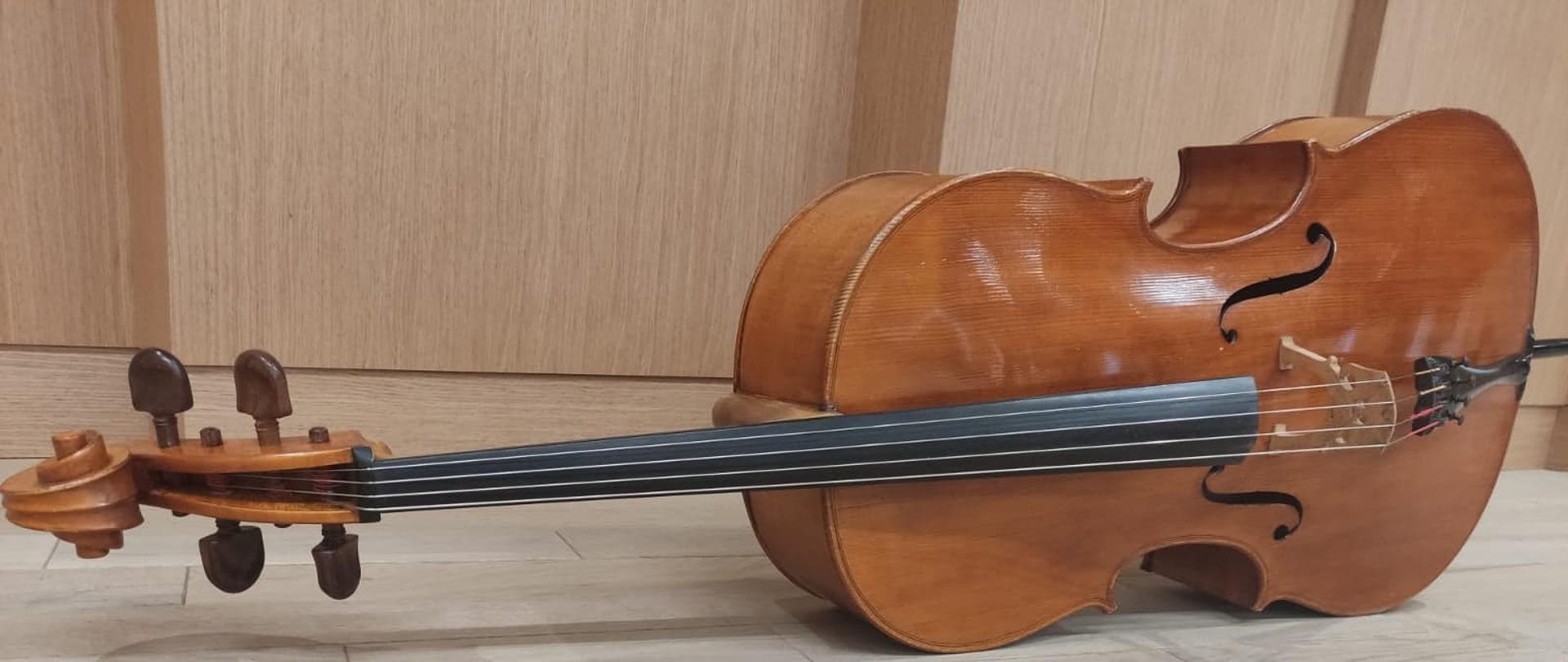 zdjęcie ukazuje wiolonczelę położoną na drewnianej podłodze