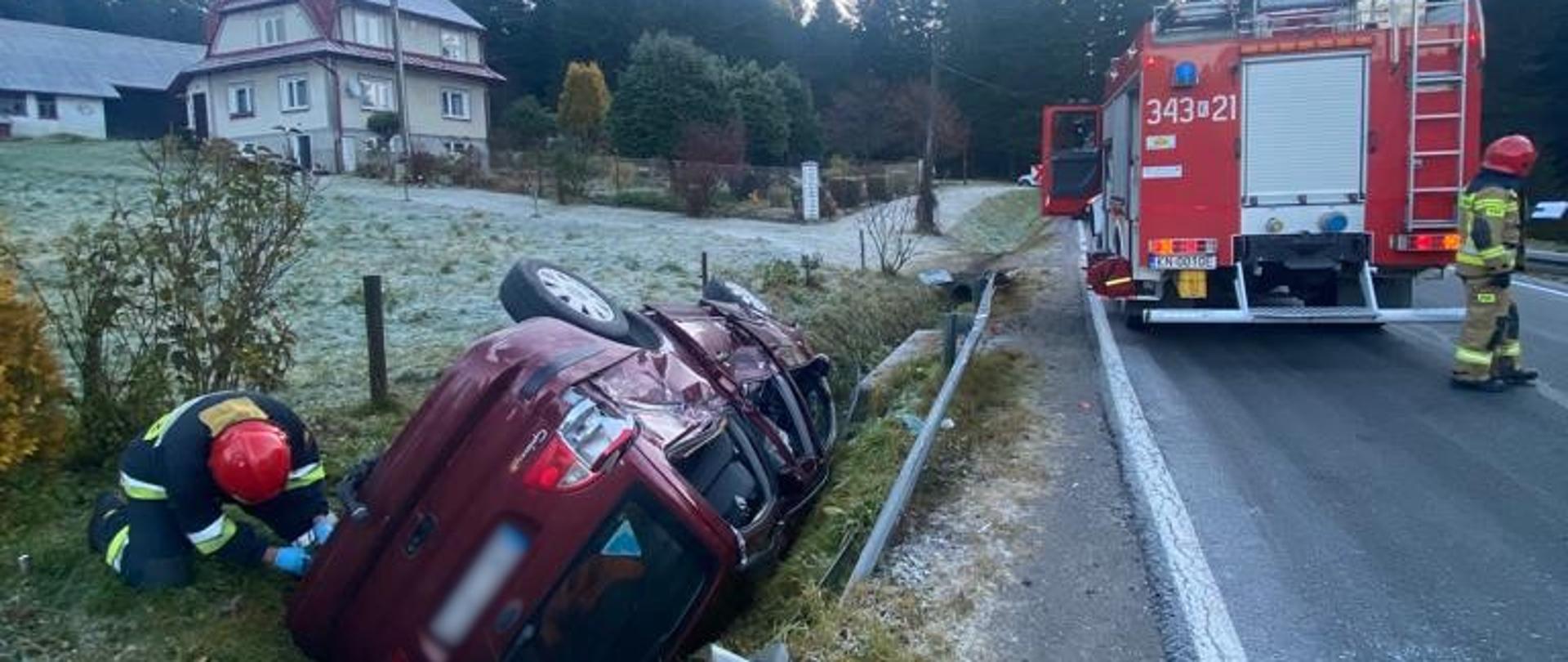 Samochód na dachu poza drogą. Samochód pożarniczy stoi na drodze.