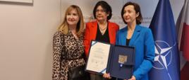 Członek KRRiT dr hab. Hanna Karp z Laureatką nagrody im. dr. Pawła Stępki ( po prawej) oraz Promotorką (po lewej) - stoją na tle logo KRRiT i flagi NATO oraz Polski