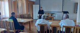 widoczni uczestnicy spotkania, druhowie OSP, oraz funkcjonariusz psp przedstawiający prezentację.