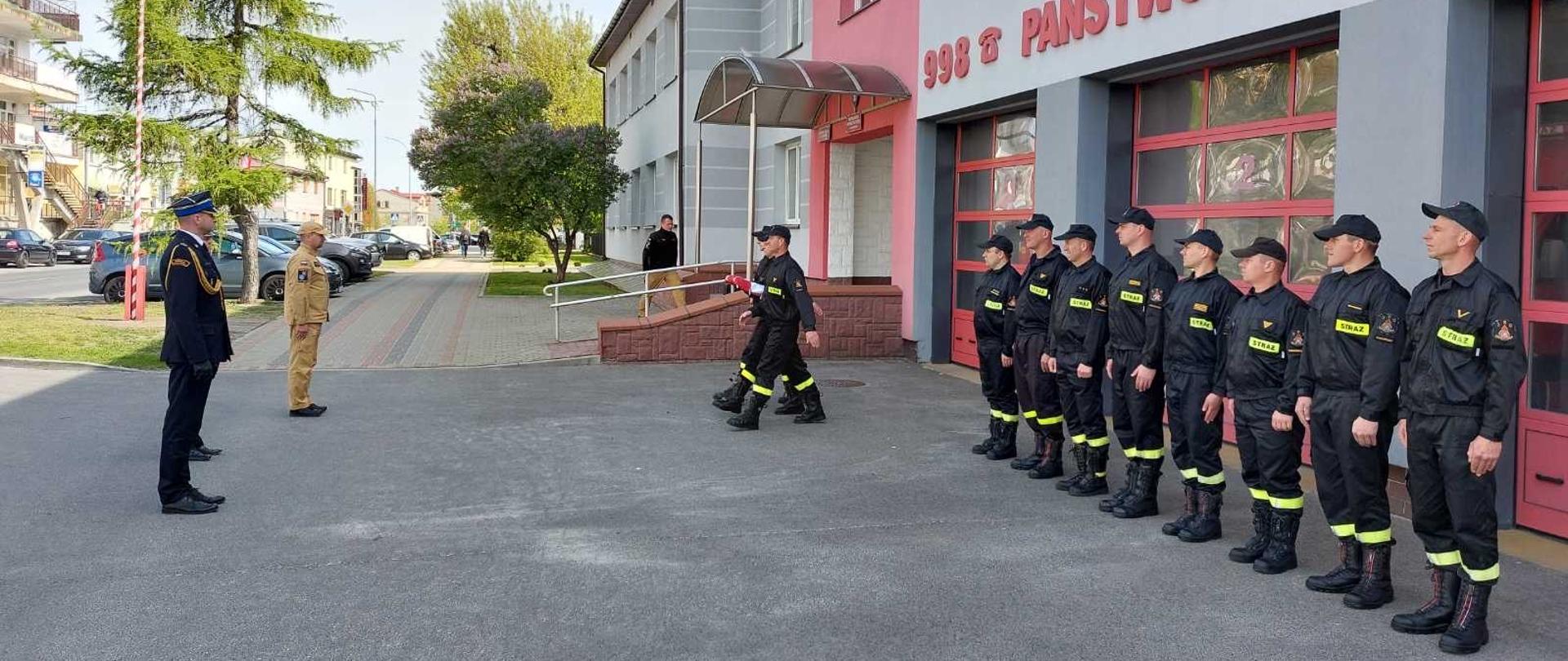 Przed budynkiem strażacy stoją na zbiórce