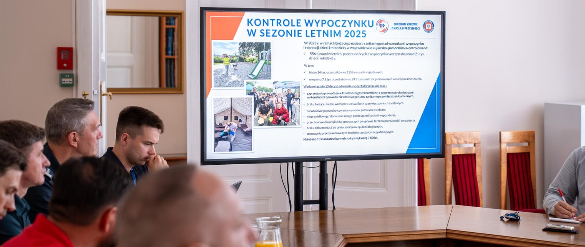 Uczestnicy spotkania w sali konferencyjnej oglądają prezentację o kontrolach wypoczynku w sezonie letnim 2025.