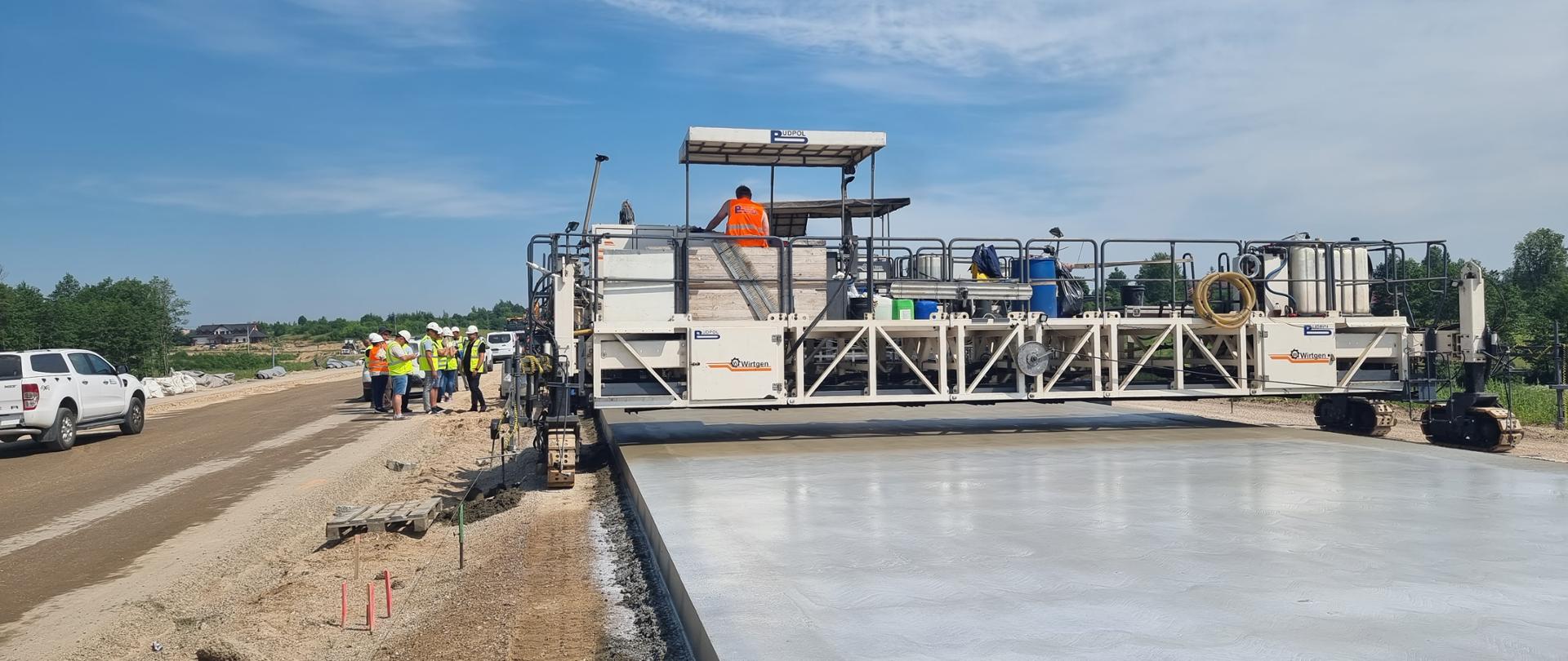 Maszyna układa szeroki pas betonu, który będzie jedną z jezdni drogi ekspresowej 