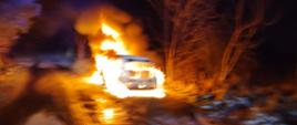 Zdjęcie przedstawia palący się samochód osobowy. Samochód całkowicie objęty pożarem. Pora nocna. 