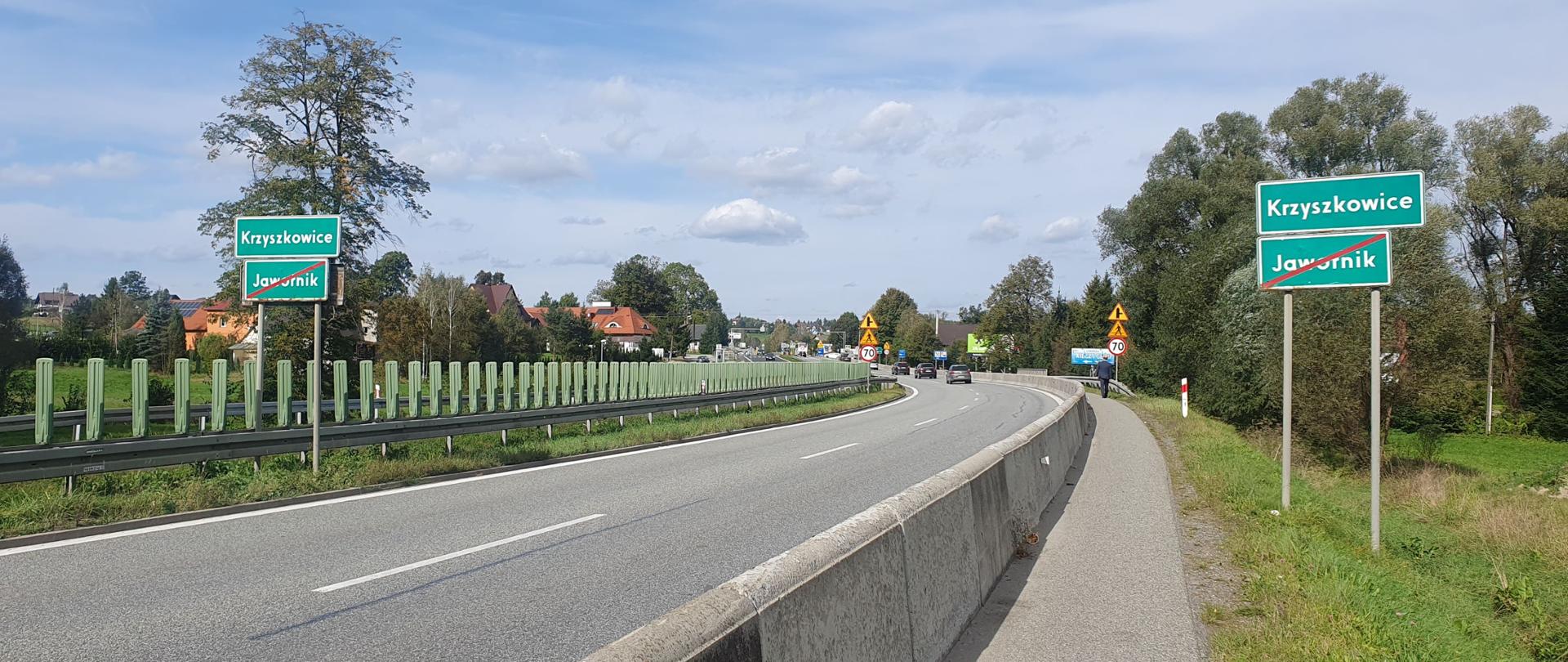 DK7 w Krzyszkowicach, pobocze oddzielone betonowymi płytami od pasów ruchu, między jezdniami bariery przeciwolśnieniowe, w oddali zabudowania miejscowości