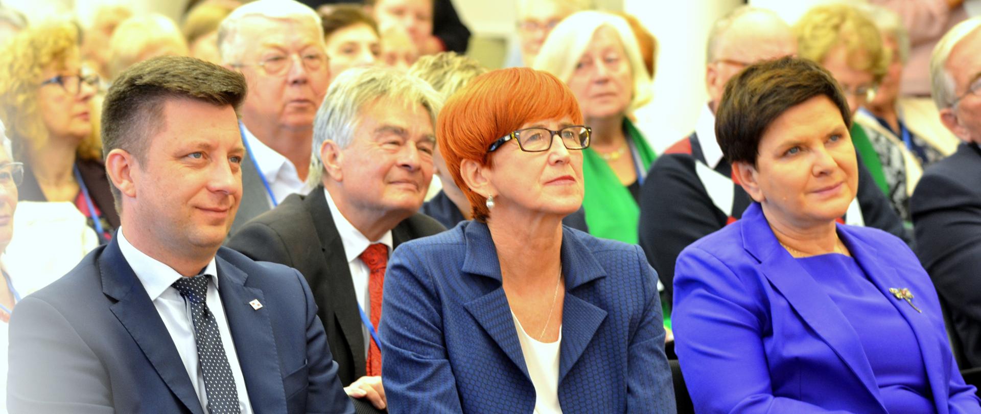 III spotkanie seniorów. Minister Elżbieta, Wicepremier Beata Szydło, Minister w Kancelarii Prezesa Rady Ministrów Michał Dworczyk oraz uczestnicy klubów senior plus słuchają wystąpień okolicznościowych podczas wydarzenia. 