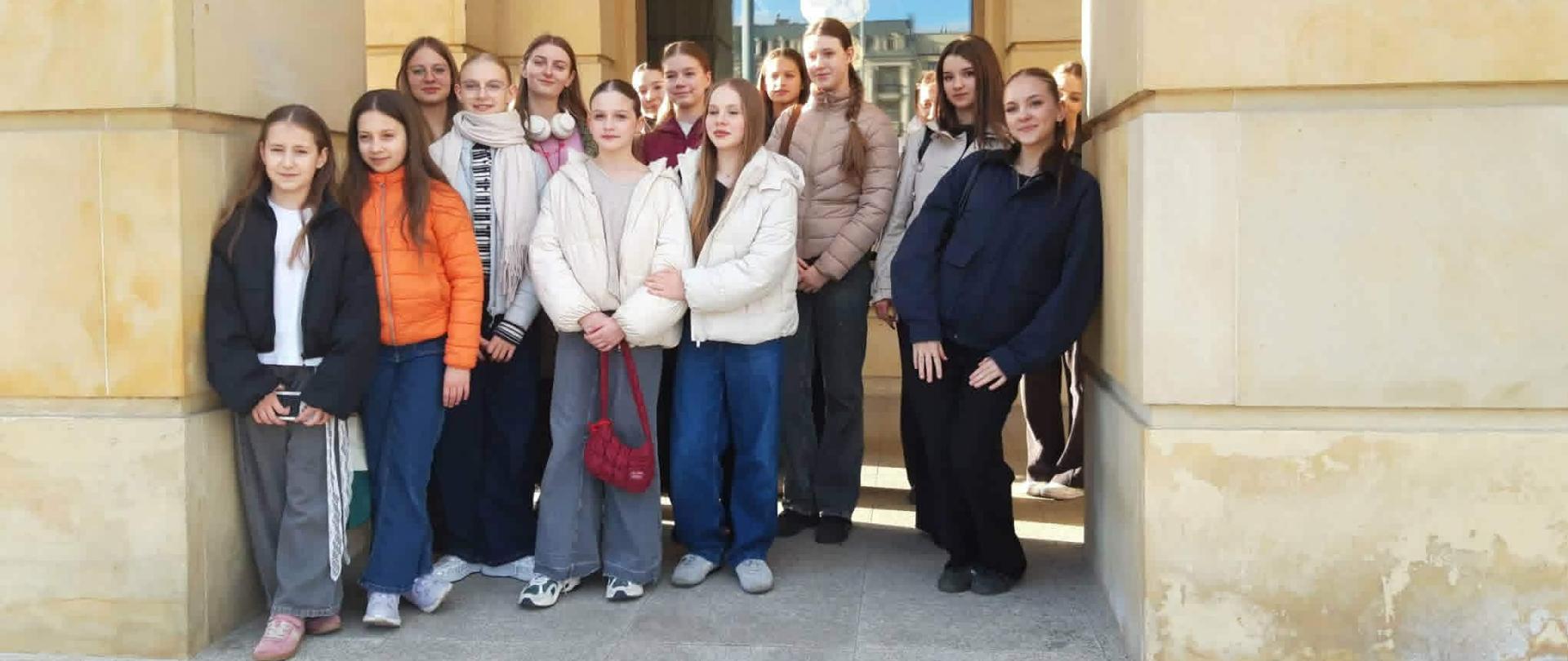 Grupa dziewcząt pozuje do zdjęcia przed budynkiem Teatru Wielkiego w Łodzi
