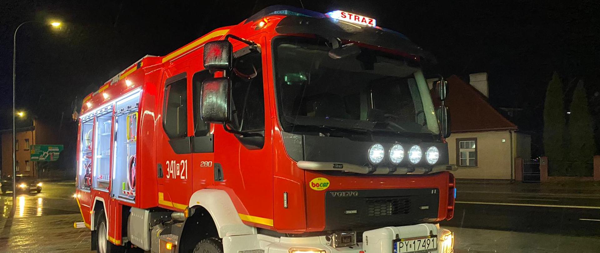 Zdjęcie wykonane w porze nocnej. Widać nowy pojazd ratowniczo-gaśniczy w kolorze czerwonym. Stoi na kostce brukowej przed garażami JRG 1 Kalisz.