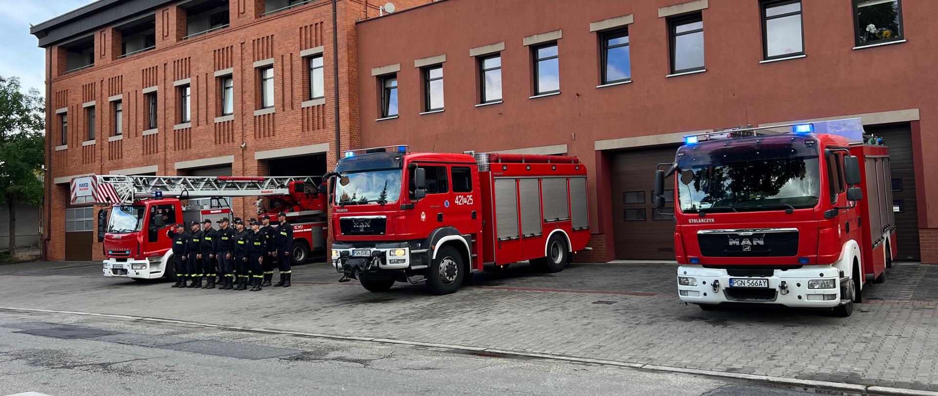 Trzy wozy strażackie oraz strażacy stojący przed garażem Komendy Powiatowej Państwowej Straży Pożarnej w Gnieźnie