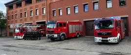 Trzy wozy strażackie oraz strażacy stojący przed garażem Komendy Powiatowej Państwowej Straży Pożarnej w Gnieźnie 