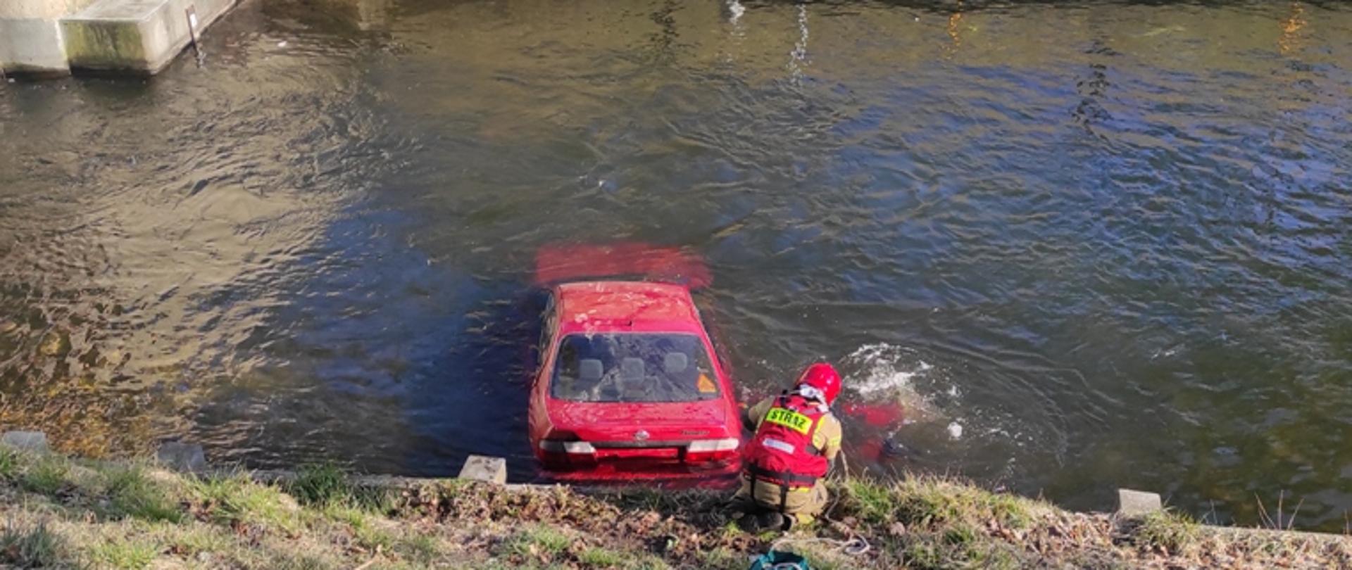 Strażacy sprawdzają czy nikogo nie ma w samochodzie, który wpadł do kanału. 