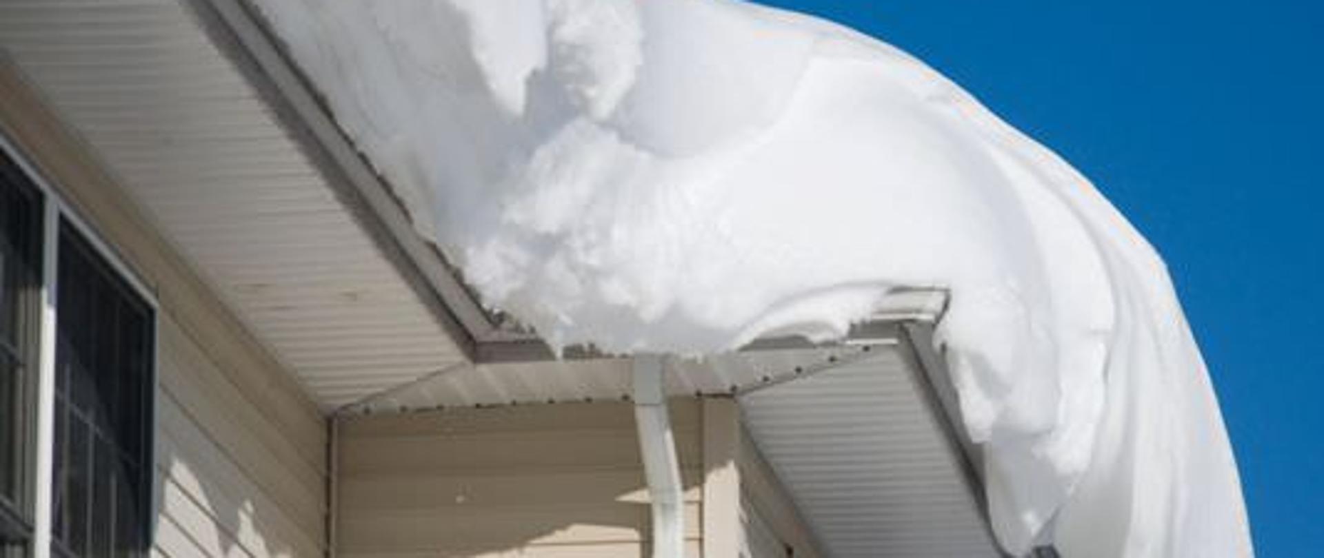 Duża ilość śniegu leży na dachu budynku o jasnych ścianach i podbitce