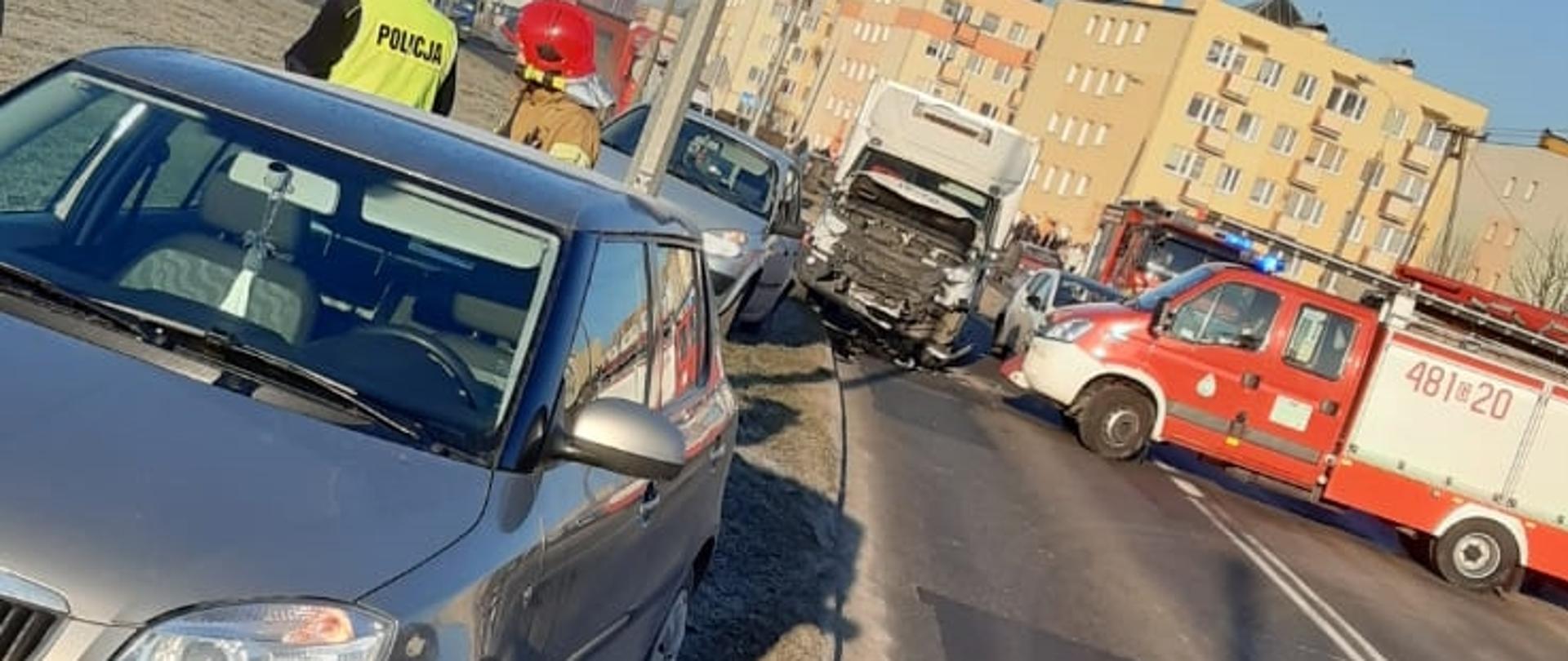 Fotografia przedstawia trzy rozbite samochody osobowe na poboczu drogi przy których działania prowadzą strażacy oraz policjanci. 