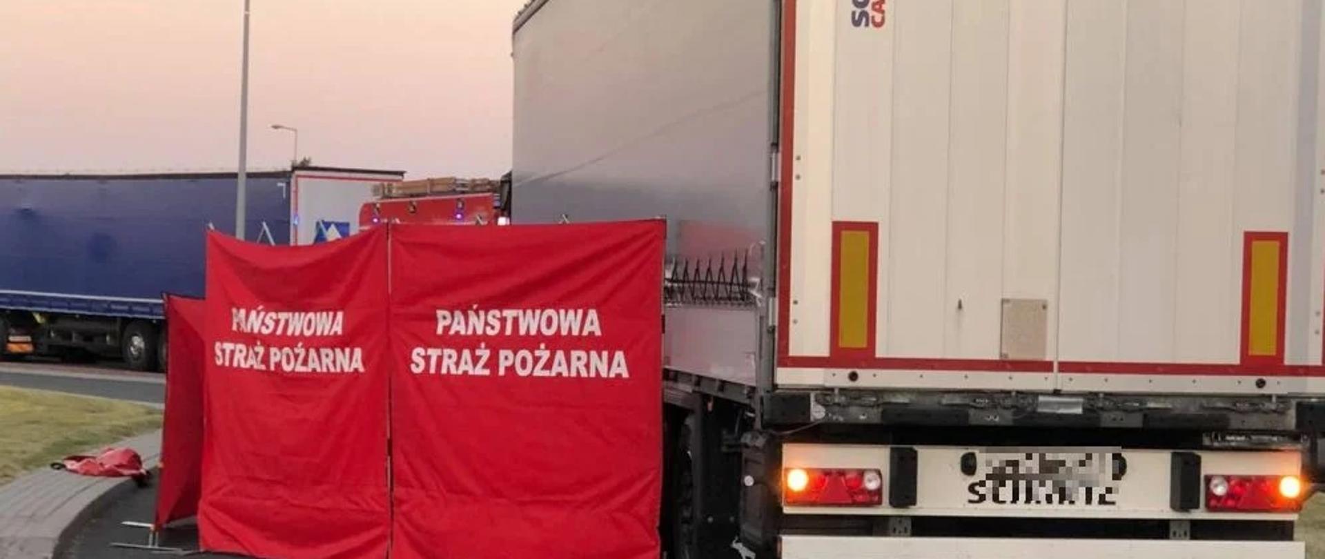 Zdjęcie przedstawia samochód ciężarowy otoczony czerwonym parawanem.