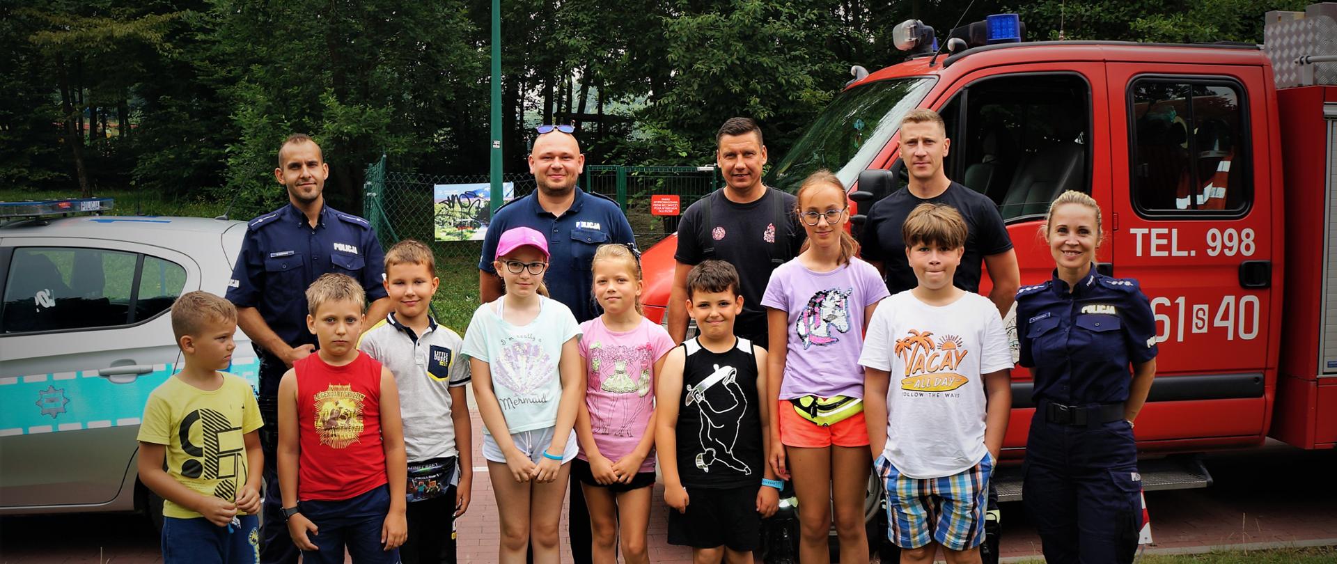 Na zdjęciu strażacy i policjanci na tle samochodów wraz z dziećmi
