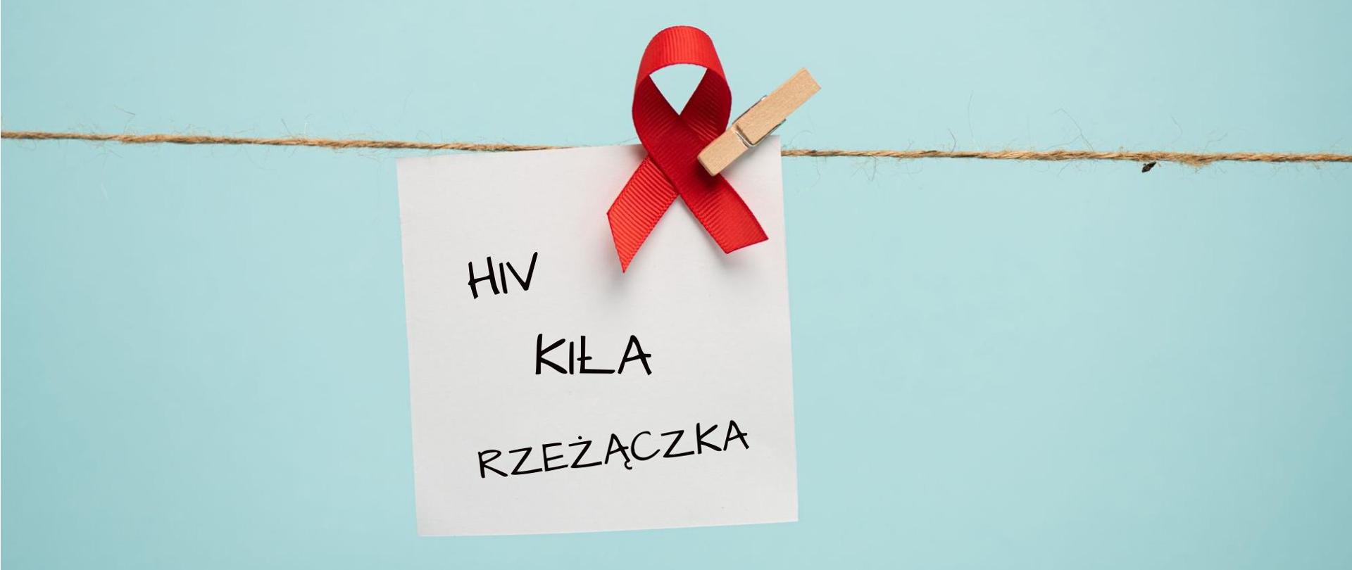 Na zdjęciu w centrum jest karteczka na której jest napisane: HIV, kiła, rzeżączka. Powyżej widać czerwoną wstążkę. Kartka wisi na sznurku. Tło jest błękitne.