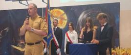 Na zdjęciu Komendant Powiatowy PSP w Pruszczu Gdańskim w tle uczniowie prowadzący uroczystość oraz poczet sztandarowy.