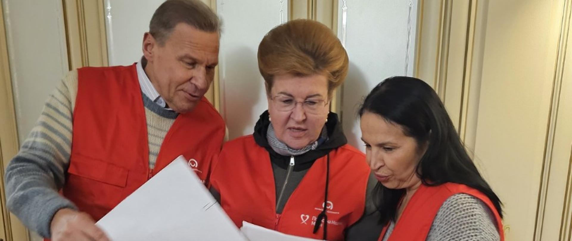 Grupa osób w kamizelkach z logo Polska pomoc przegląda dokumenty