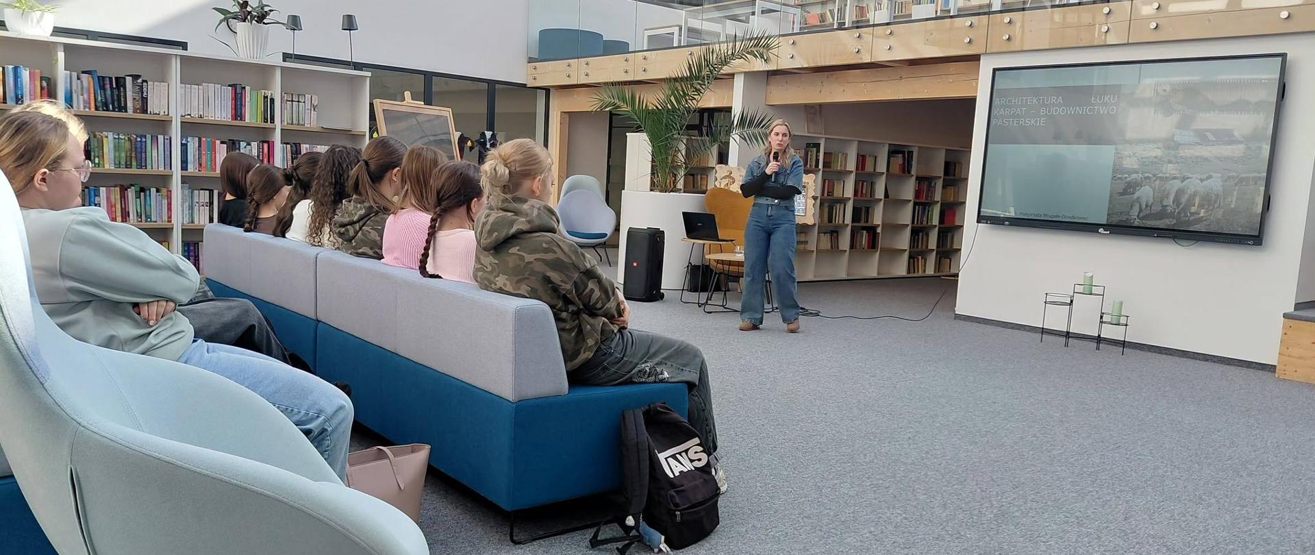 Zdjęcie kobiety przemawiającej przed grupą uczniów w bibliotece