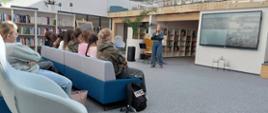 Zdjęcie kobiety przemawiającej przed grupą uczniów w bibliotece