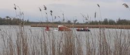 Zdjęcie przedstawia przewróconą żaglówkę na Jeziorze Pątnowskim oraz dwie łodzie ze strażakami. 