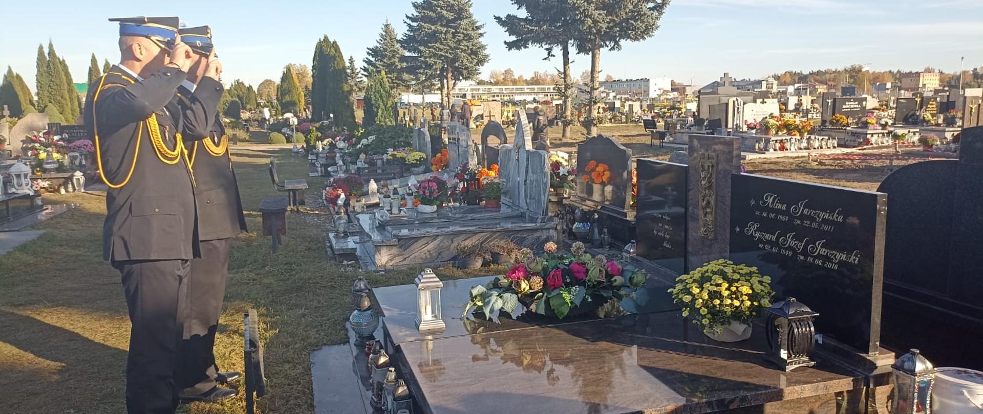 Strażacy salutujący nad grobem zmarłego funkcjonariusza.