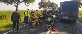 Wypadek na trasie Dłoń-Smolice. Droga krajowa nr 36 (94 kilometr). Strażacy udzielają kwalifikowanej pierwszej pomocy rannemu kierowcy mercedesa sprintera, który leży na jezdni. Z lewej strony stoi dwóch policjantów ruchu drogowego. Z prawej - pojazdu uczestniczące w zdarzeniu. W tle wóz straży pożarnej, pole kukurydzy oraz drzewa.