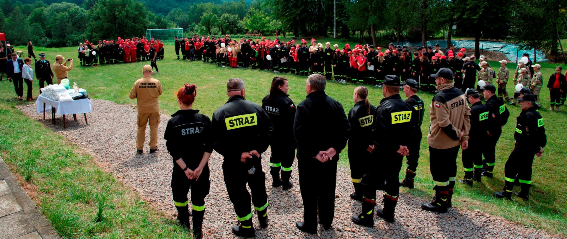 Widok ogólny. Zbiórka uczestników rajdu na boisku. Na pierwszym planie - tyłem – komisja sędziowska, w głębi wszystkie drużyny MDP, po lewej stronie stolik z nagrodami.