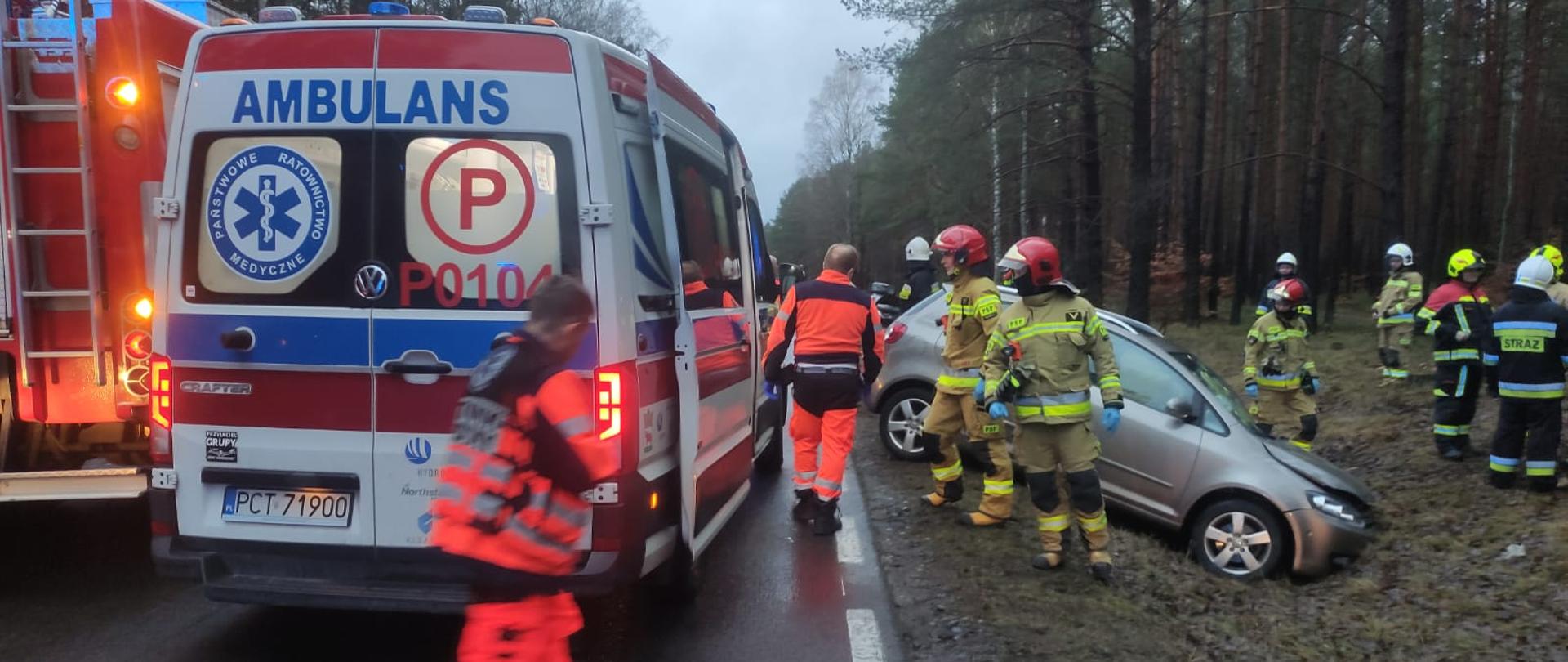 Strażacy i ratownicy wokół samochodu w rowie.