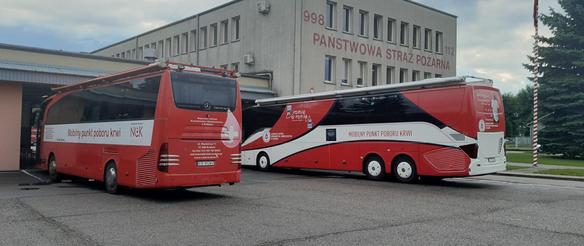 Dwa czerwone autobusy staja przed garażami JRG1. Na autobusach widnieje napis MOBILNY PUNKT POBORU KRWI