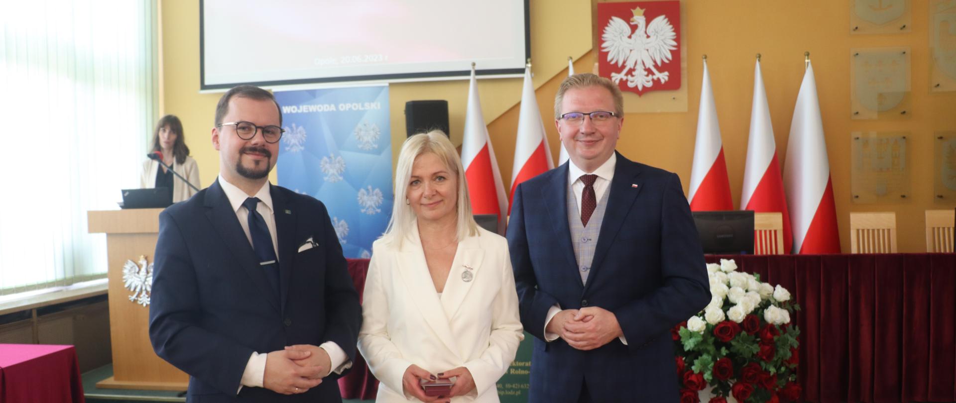 Kobieta trzyma odznaczenie i dwóch mężczyzn 