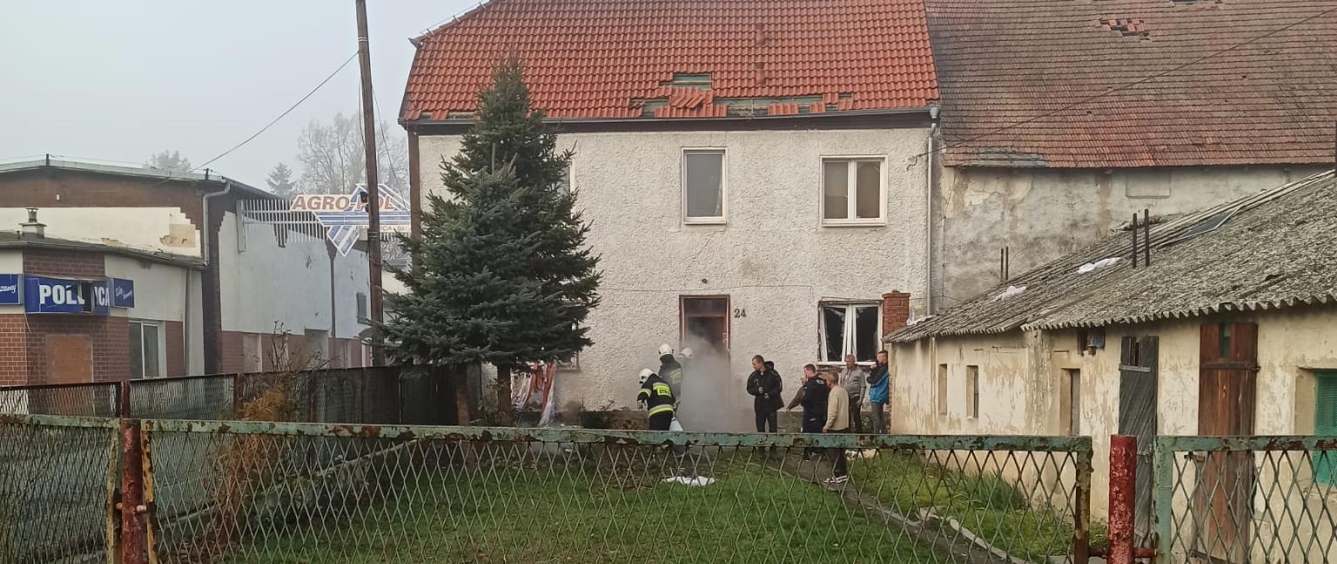 na zdjęciu widać częściowo zniszczony po wybuchu gazu budynek wielorodzinny. Przed budynkiem znajdują się mieszkańcy i strażacy.