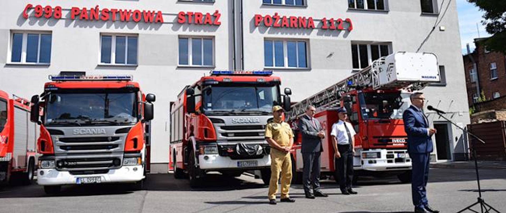 Na zdjęciu znajdują się przemawiający wojewoda śląski Jarosław Wieczorek, za nim śląski komendant wojewódzki PSP nadbryg. Jacek Kleszczewski, poseł na Sejm RP Marek Wesoły oraz komendant miejski st. bryg. Andrzej Małysiak. W tle znajdują się samochody ratowniczo gaśnicze.
