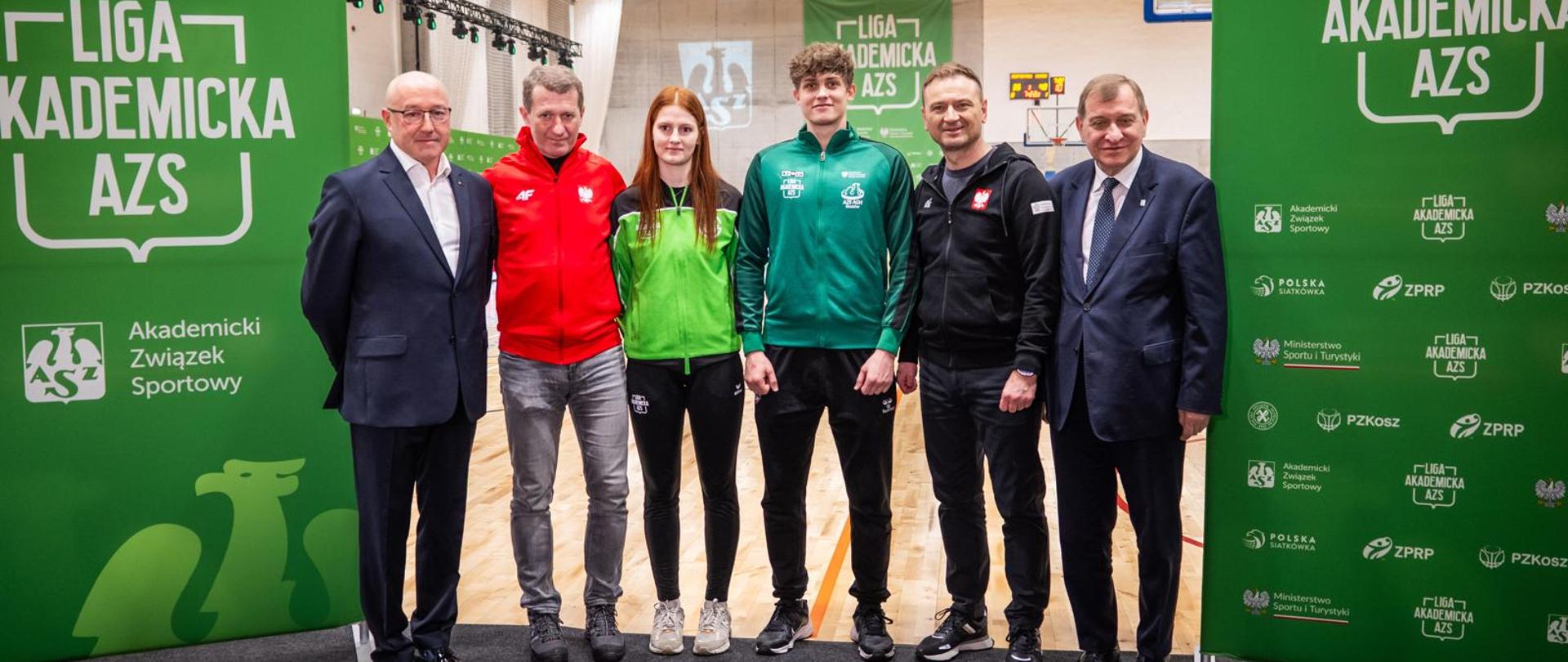 Zdjęcie uczestników konferencji prasowej na hali Akademii Górniczo-Hutniczej, gdzie odbywały się wielkie finały Lig Akademickich AZS w koszykówce, piłce ręcznej i siatkówce. W tle mecz koszykówki. Po lewej lewej i prawej stronie rollupy m.in. z dużym napisem Liga Akademicka AZS i logiem MSiT.