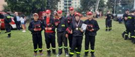 członkowie MDP Świerże Górne w trakcie I Młodzieżowych Mistrzostw Mazowsza w Ochronie Ludności stoją na boisku sportowym trzymając nagrody, obok inni zawodnicy