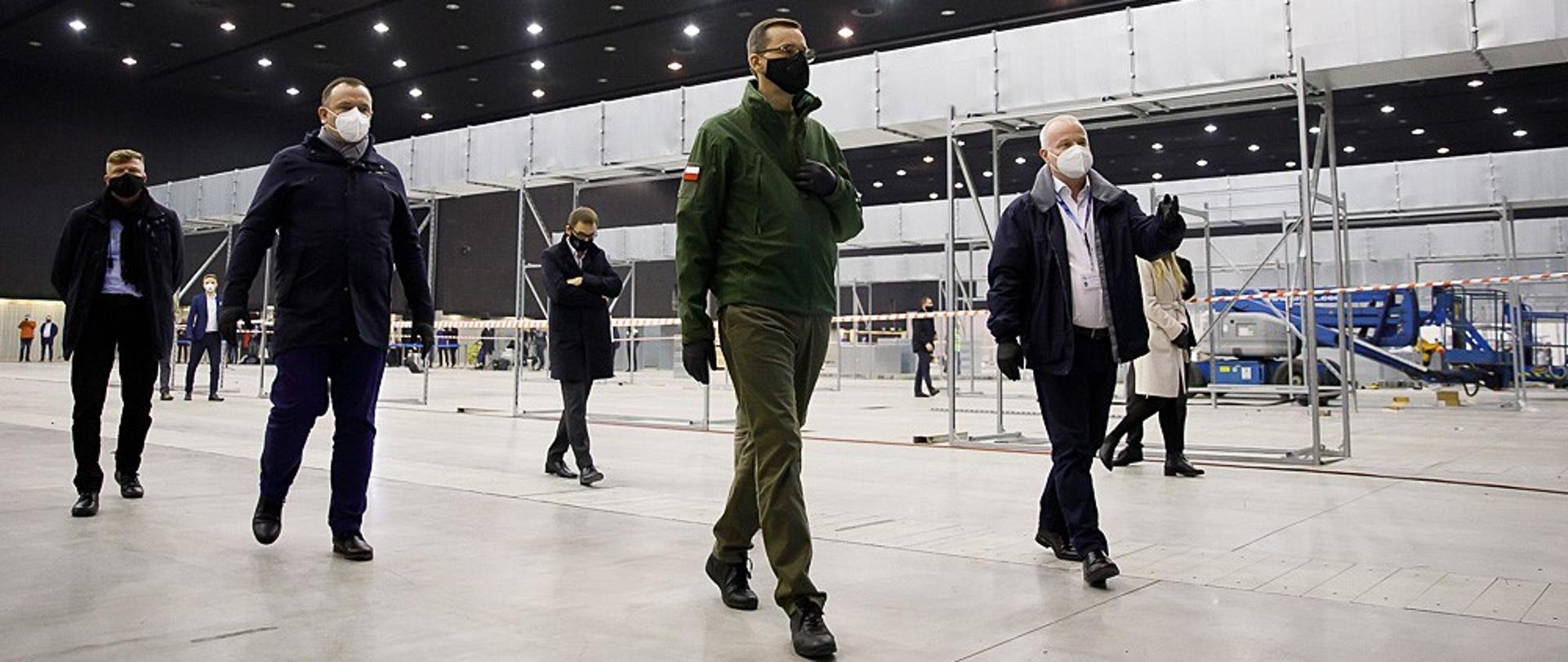 Premier Mateusz Morawiecki idzie po terenie budowy szpitala tymczasowego.