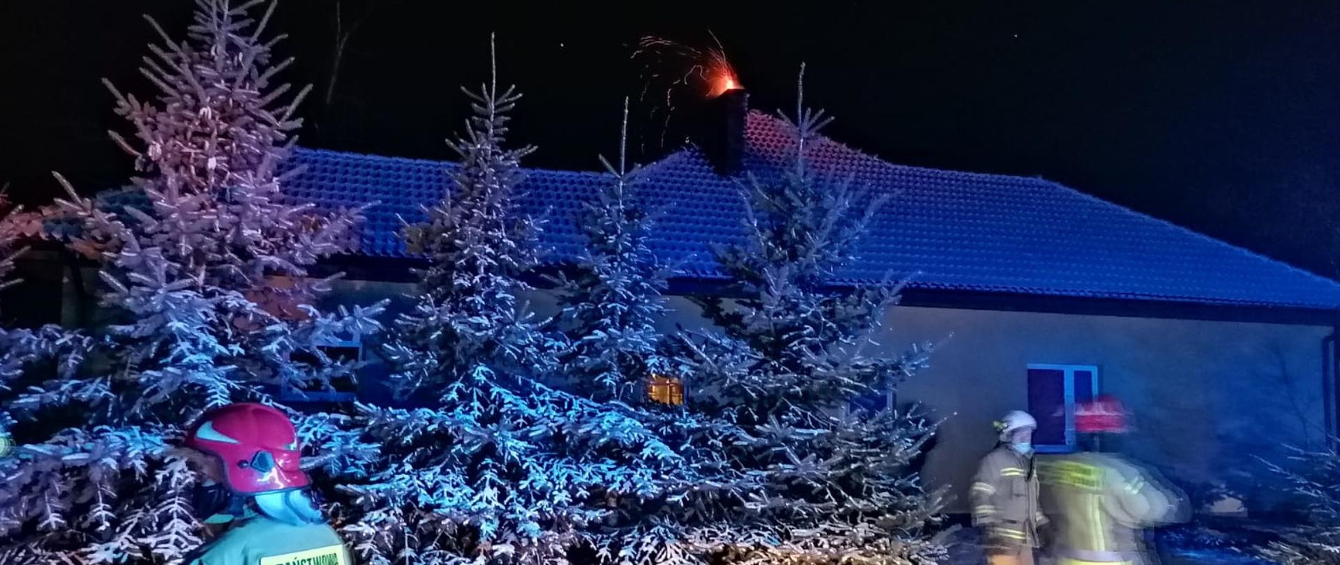 Budynek objęty działaniami widoczni strażacy komin z płonącą sadzą.