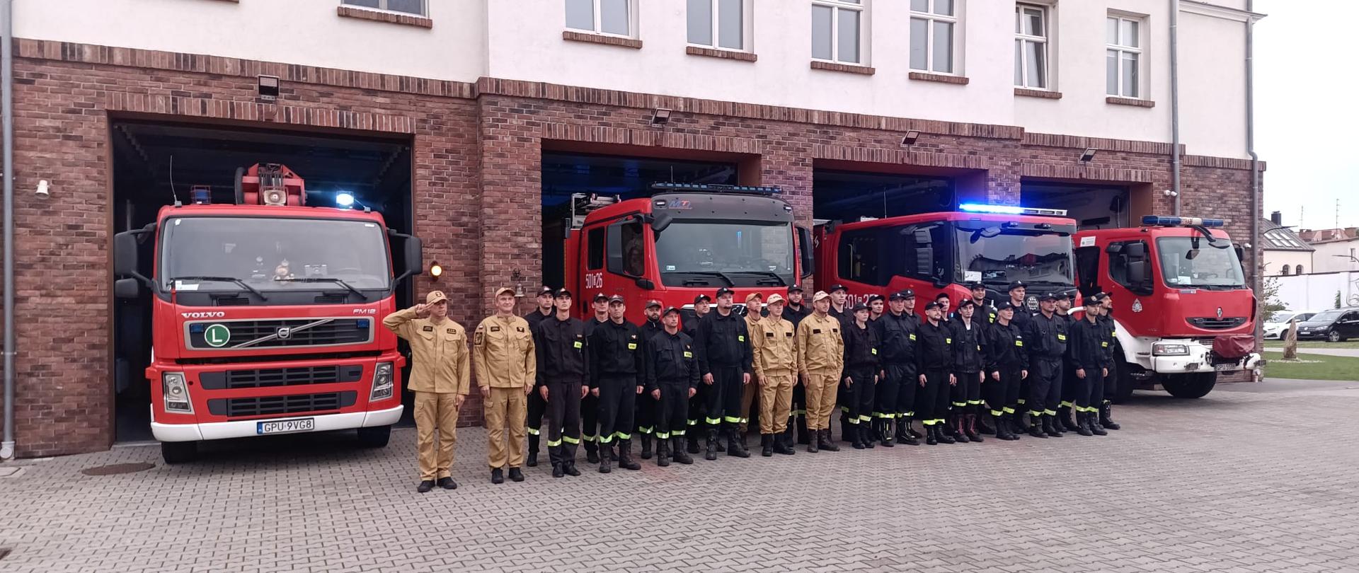 Funkcjonariusze z JRG w Pucku oraz druhny i druhowie z Ochotniczych Straży Pożarnych Powiatu Puckiego oddają hołd tragicznie zmarłemu druhowi z OSP Michałów. Strażacy są ustawieni w dwuszeregu, ubrani w koszarowe. Na drugim planie wozy bojowe JRG Puck oraz budynek JRG
