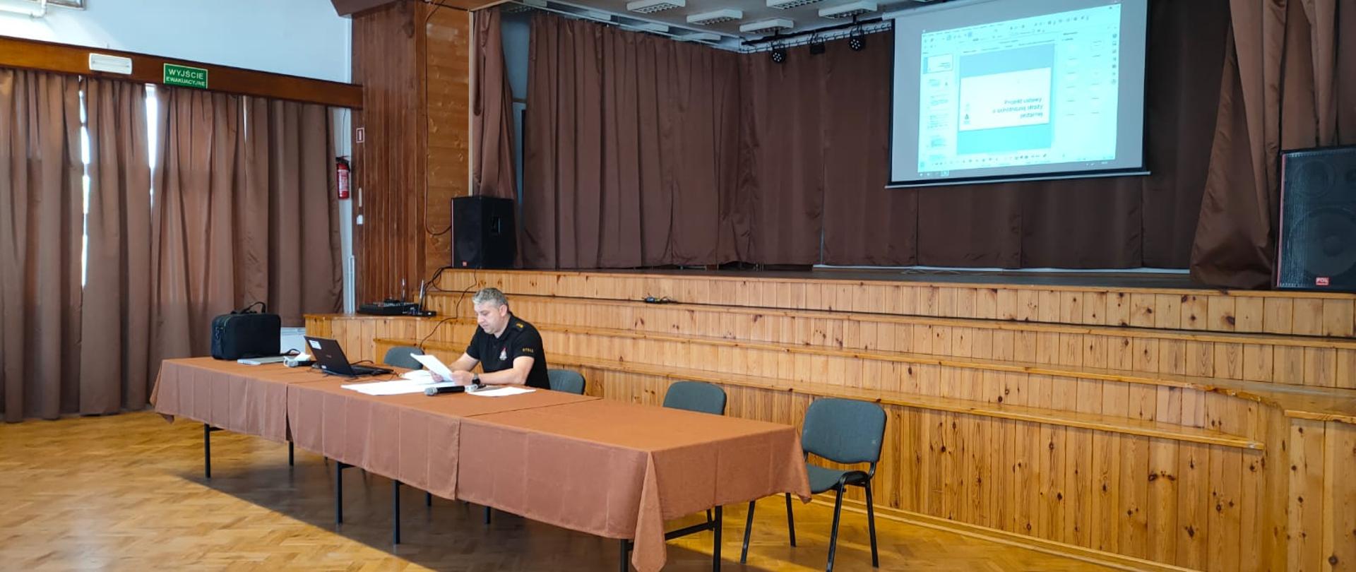 strażak siedzący za stołem na sali widowiskowej trzymający w ręce kartki papieru