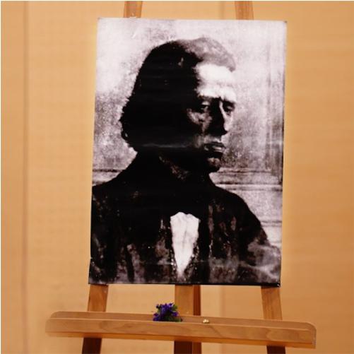 Grafika przedstawia sztalugę, na której ustawiony jest portret Fryderyka Chopina