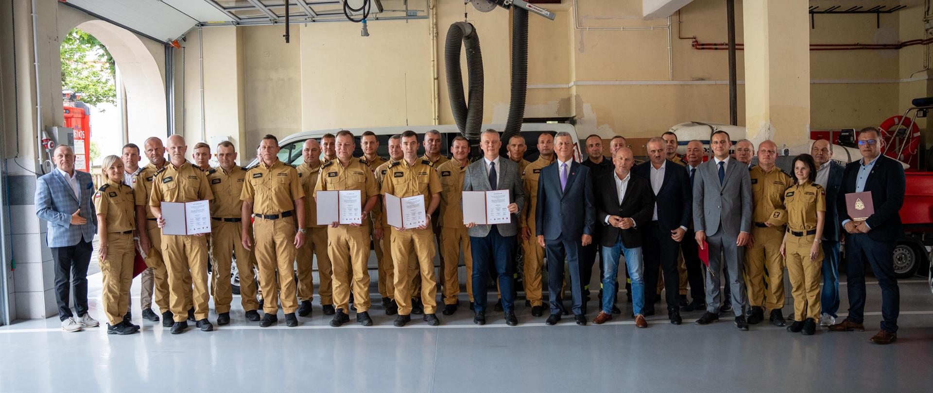 Grupowe zdjęcie w garażu jednostki, sygnatariusze prezentują podpisany list