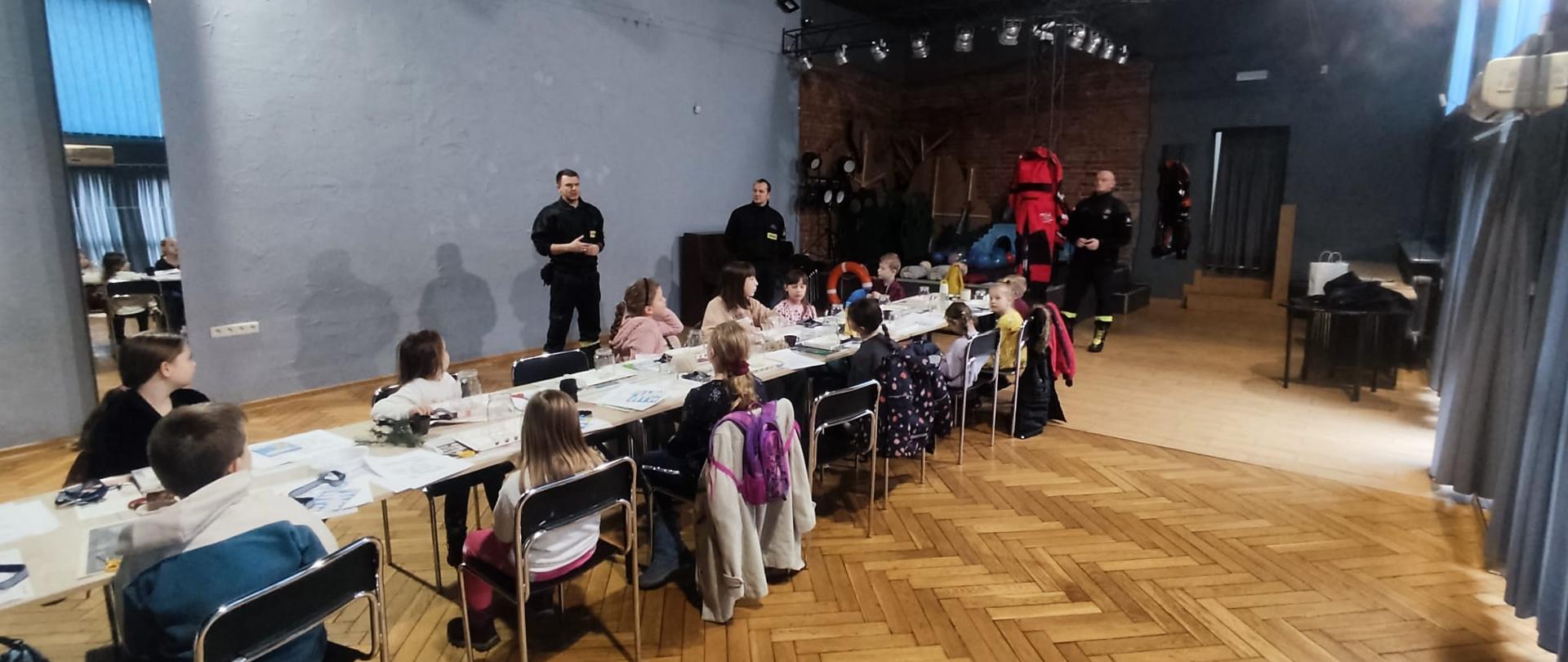 Dzieci słuchają prelekcji strażaków na temat bezpieczeństwa podczas ferii zimowych