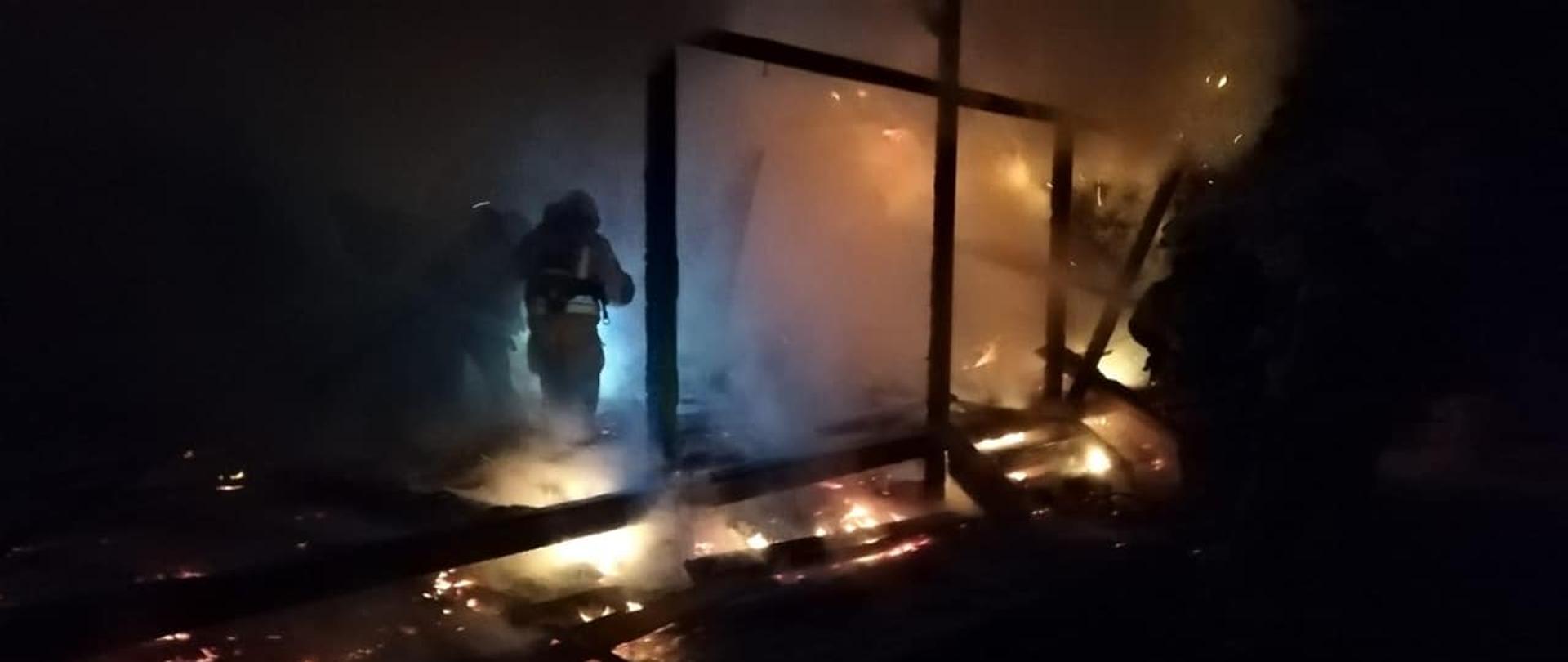 Na zdjęciu widzimy strażaków wchodzących do budynku letniskowego objętego pożarem.