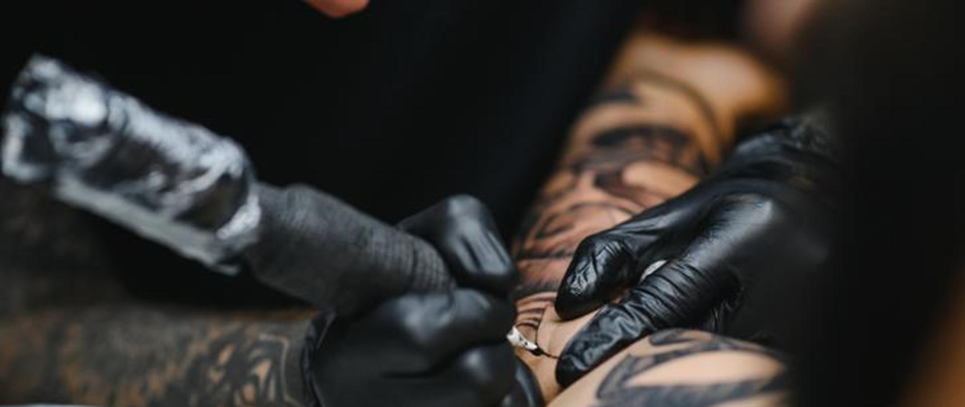 Na zdjęciu przedstawiono dłonie tatuażysty wykonującego tatuaż.